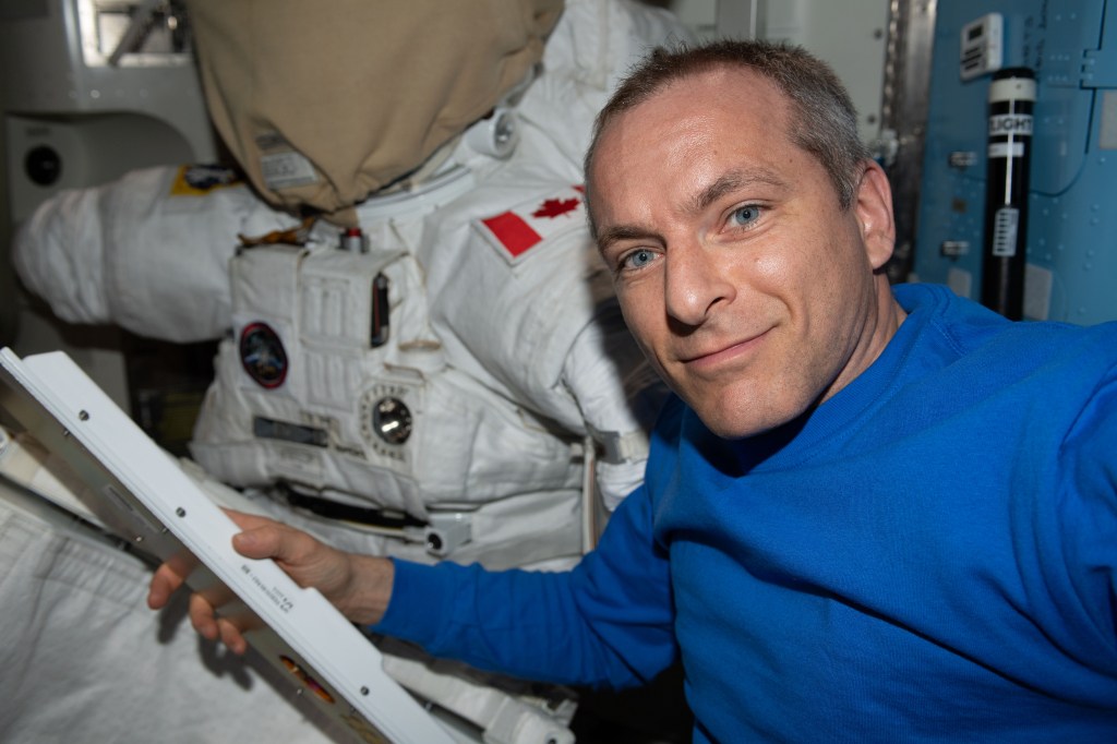 iss058e002219 (Jan. 5, 2019) --- Canadian Space Agency astronaut David Saint-Jacques works on U.S. spacesuit maintenance in the Quest airlock. A spacesuit with a patch of the flag of Canada on the left shoulder is seen behind Saint-Jacques. Spacewalks conducted in U.S. spacesuits are staged in Quest.