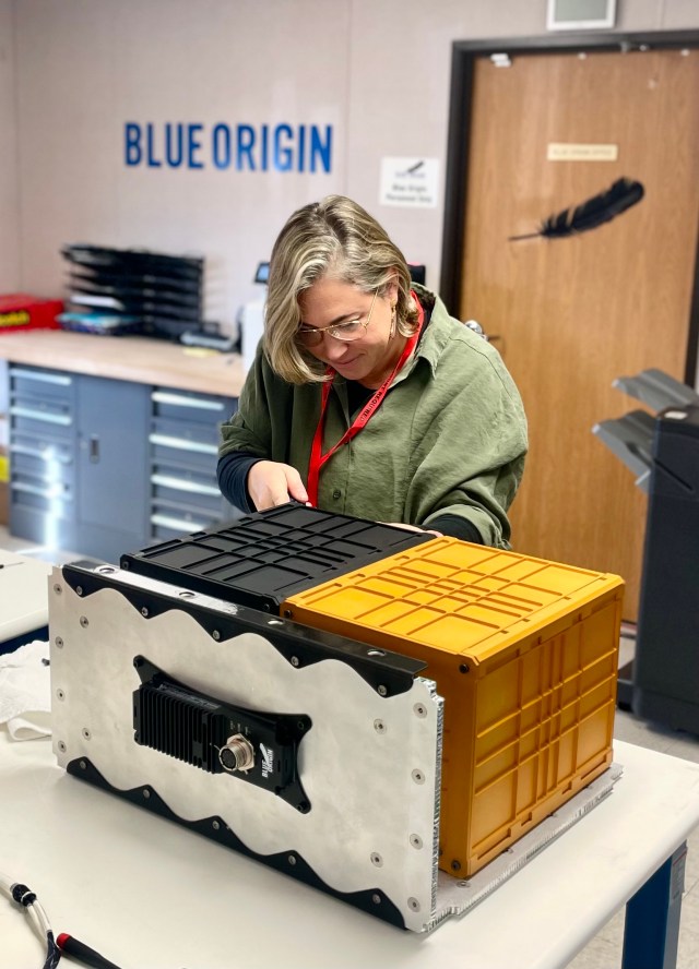 Female researcher leans over a gold and black box on a work table.