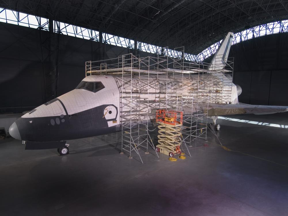 Lo Space Shuttle Enterprise viene sottoposto a restauro presso lo Stephen F. Udvar-Hazy Center del National Air and Space Museum (NASM) dello Smithsonian Institution a Chantilly, Virginia. Da notare il bordo d'attacco dell'ala mancante, donato per le indagini sull'incidente della Columbia