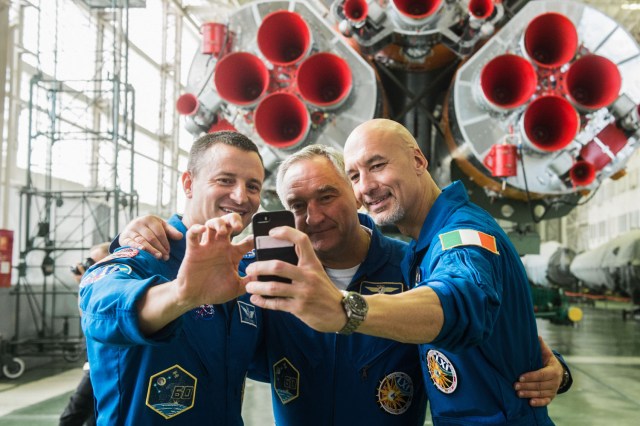 jsc2019e039431 (July 16, 2019) --- In the Integration Building at the Baikonur Cosmodrome in Kazakhstan, Expedition 60 crewmembers Drew Morgan of NASA (left), Alexander Skvortsov of Roscosmos (center) and Luca Parmitano of the European Space Agency (right) pose for a selfie in front of the first stage engines of their Soyuz booster July 16 as part of pre-launch preparations. They will launch July 20 on the Soyuz MS-13 spacecraft from the Baikonur Cosmodrome for a mission on the International Space Station. Credit: Andrey Shelepin/GCTC