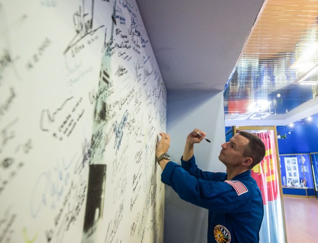 jsc2019e039428 (July 16, 2019) --- At the Baikonur Cosmodrome in Kazakhstan, Expedition 60 crewmember Drew Morgan of NASA signs a wall mural July 16 as part of pre-launch preparations. Morgan, Luca Parmitano of the European Space Agency and Alexander Skvortsov of Roscosmos will launch July 20 on the Soyuz MS-13 spacecraft from the Baikonur Cosmodrome for a mission on the International Space Station. Credit: Andrey Shelepin/GCTC