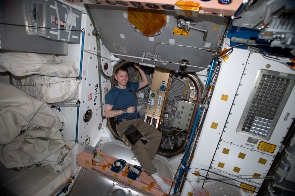iss060e021455 (Aug. 5, 2019) --- Expedition 60 Flight Engineer Nick Hague of NASA is pictured in the vestibule between the Unity module and the Northrop Grumman Cygnus space freighter. Hague had installed a SlingShot Deployer to the outside of Cygnus' hatch that would eject several small satellites once the commercial cargo craft reached a safe distance from the station after its departure.