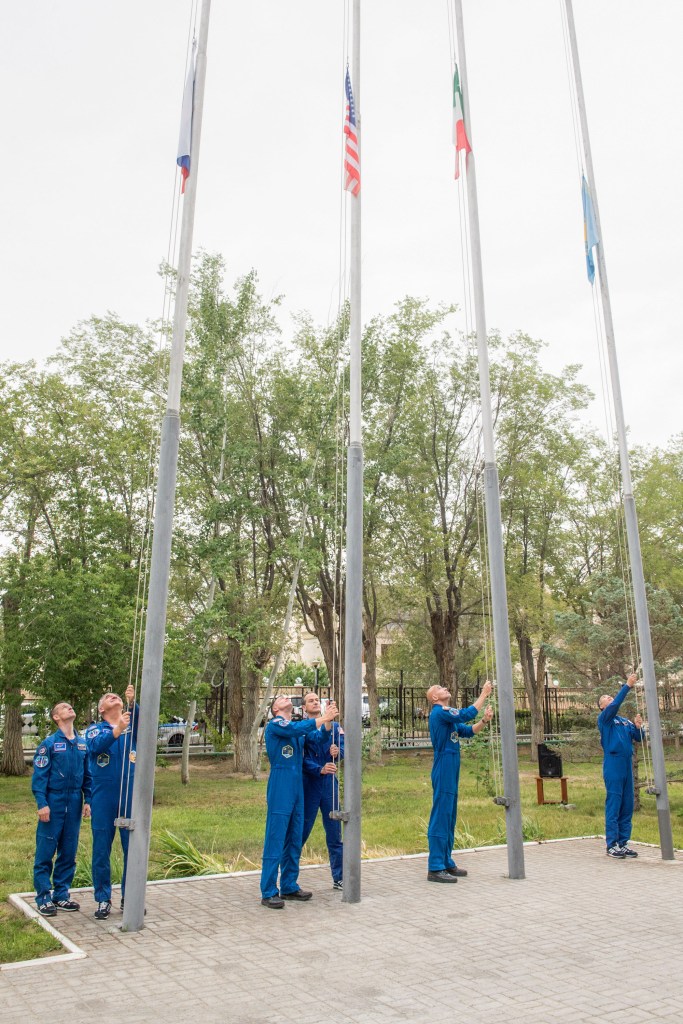 jsc2019e038396 (July 6, 2019) --- At their Cosmonaut Hotel crew quarters in Baikonur, Kazakhstan, Expedition 60 prime and backup crewmembers Sergey Ryzhikov and Alexander Skvortsov of Roscosmos, Drew Morgan and Tom Marshburn of NASA, Luca Parmitano of the European Space Agency and Soichi Noguchi of the Japan Aerospace Exploration Space Agency raise the flags of Russia, the United States, Italy and Kazakhstan in a traditional ceremony July 6. Morgan, Parmitano and Skvortsov will launch July 20 on the Soyuz MS-13 spacecraft from the Baikonur Cosmodrome in Kazakhstan for a mission on the International Space Station. Credit: Andrey Shelepin/GCTC