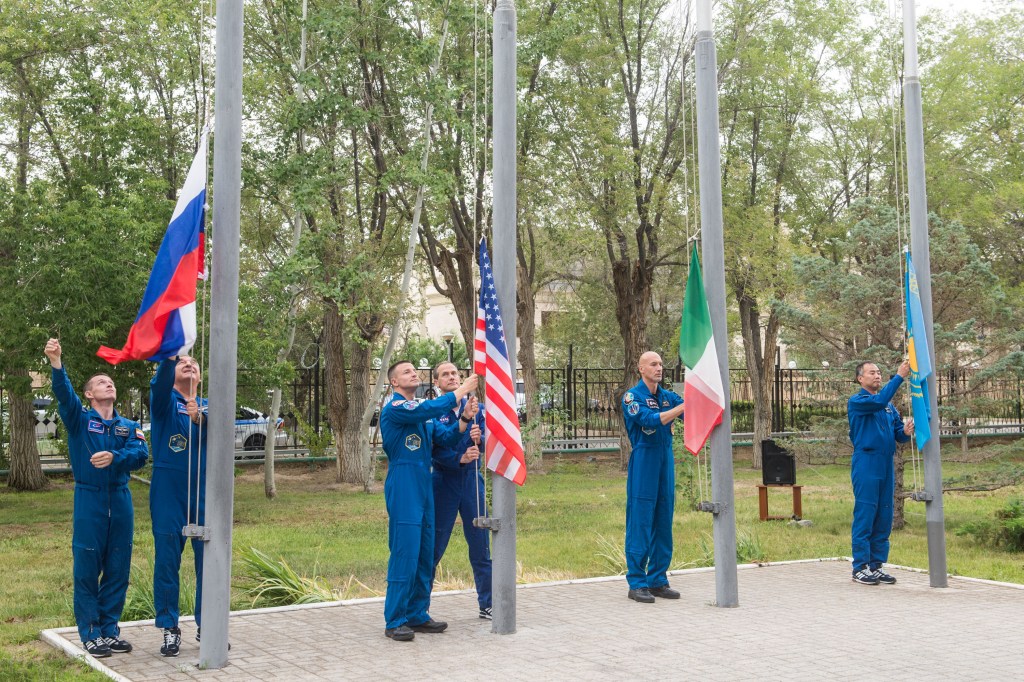 jsc2019e038395 (July 6, 2019) --- At their Cosmonaut Hotel crew quarters in Baikonur, Kazakhstan, Expedition 60 prime and backup crewmembers Sergey Ryzhikov and Alexander Skvortsov of Roscosmos, Drew Morgan and Tom Marshburn of NASA, Luca Parmitano of the European Space Agency and Soichi Noguchi of the Japan Aerospace Exploration Space Agency raise the flags of Russia, the United States, Italy and Kazakhstan in a traditional ceremony July 6. Morgan, Parmitano and Skvortsov will launch July 20 on the Soyuz MS-13 spacecraft from the Baikonur Cosmodrome in Kazakhstan for a mission on the International Space Station. Credit: Andrey Shelepin/GCTC