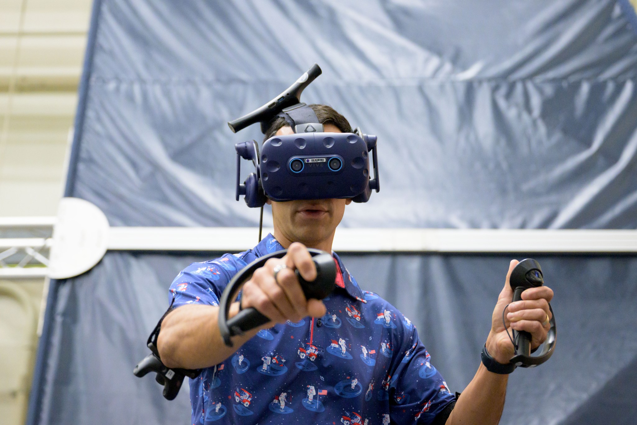 NASA Astronaut Raja Chari wearing a VR headset and holding VR controllers in both hands, immersed in training at the Virtual Reality Training Lab at NASA's Johnson Space Center.