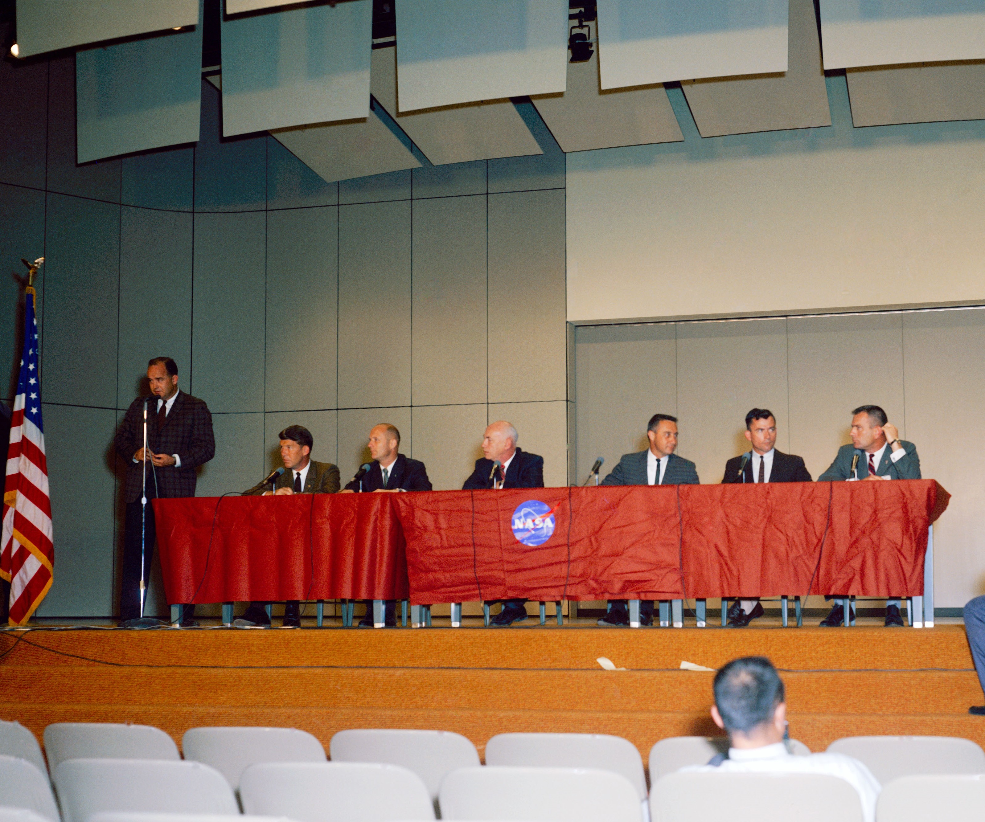 In the auditorium of the Manned Spacecraft Center (MSC), now NASA's Johnson Space Center in Houston, MSC Director Robert R. Gilruth introduces the Gemini 3 crew to the press