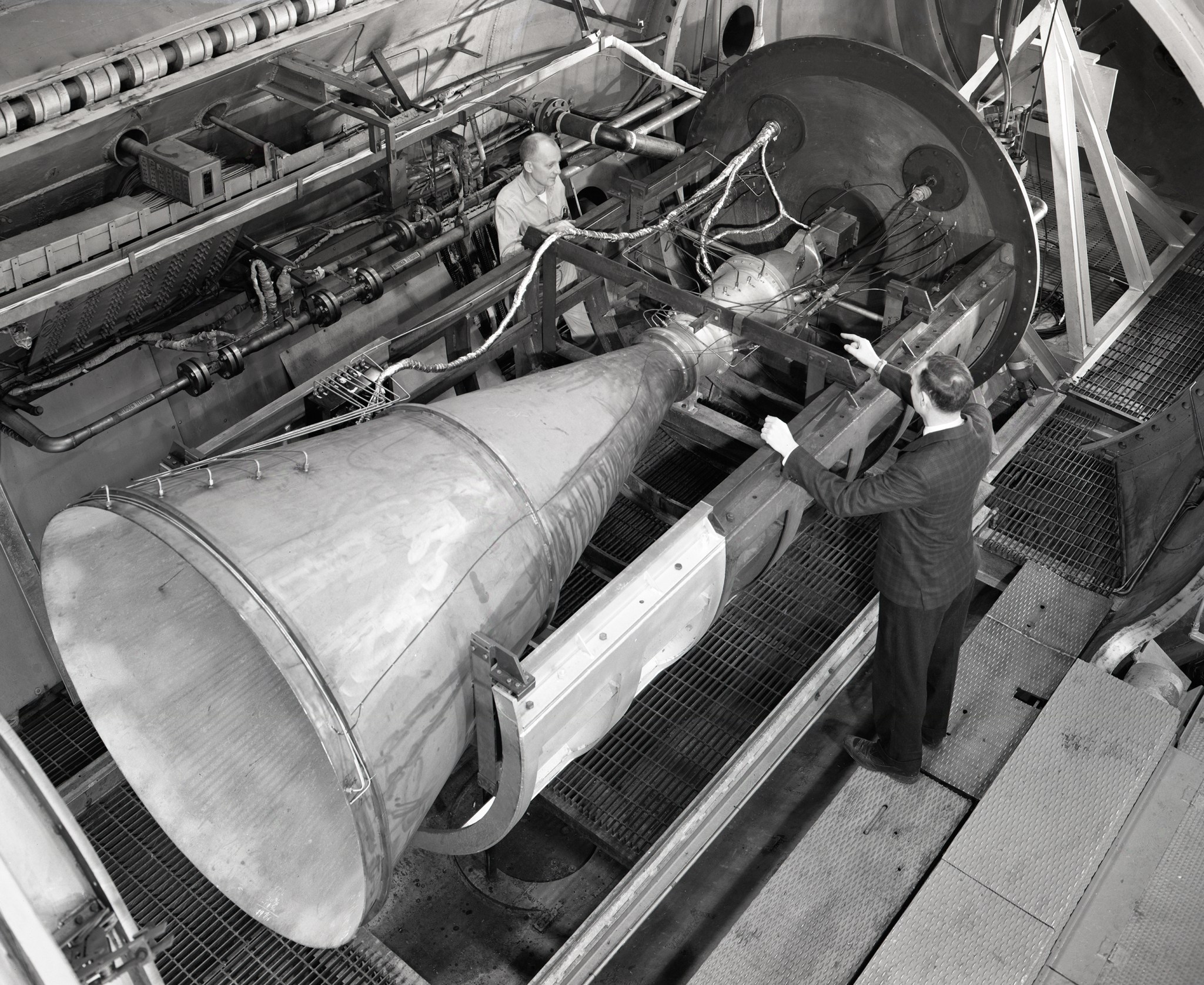 Men looking at large nozzle in test chamber.