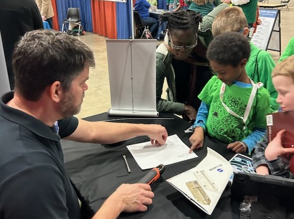 A NASA representative guides four grade-school children in a hands-on activity demonstrating shape memory alloys.