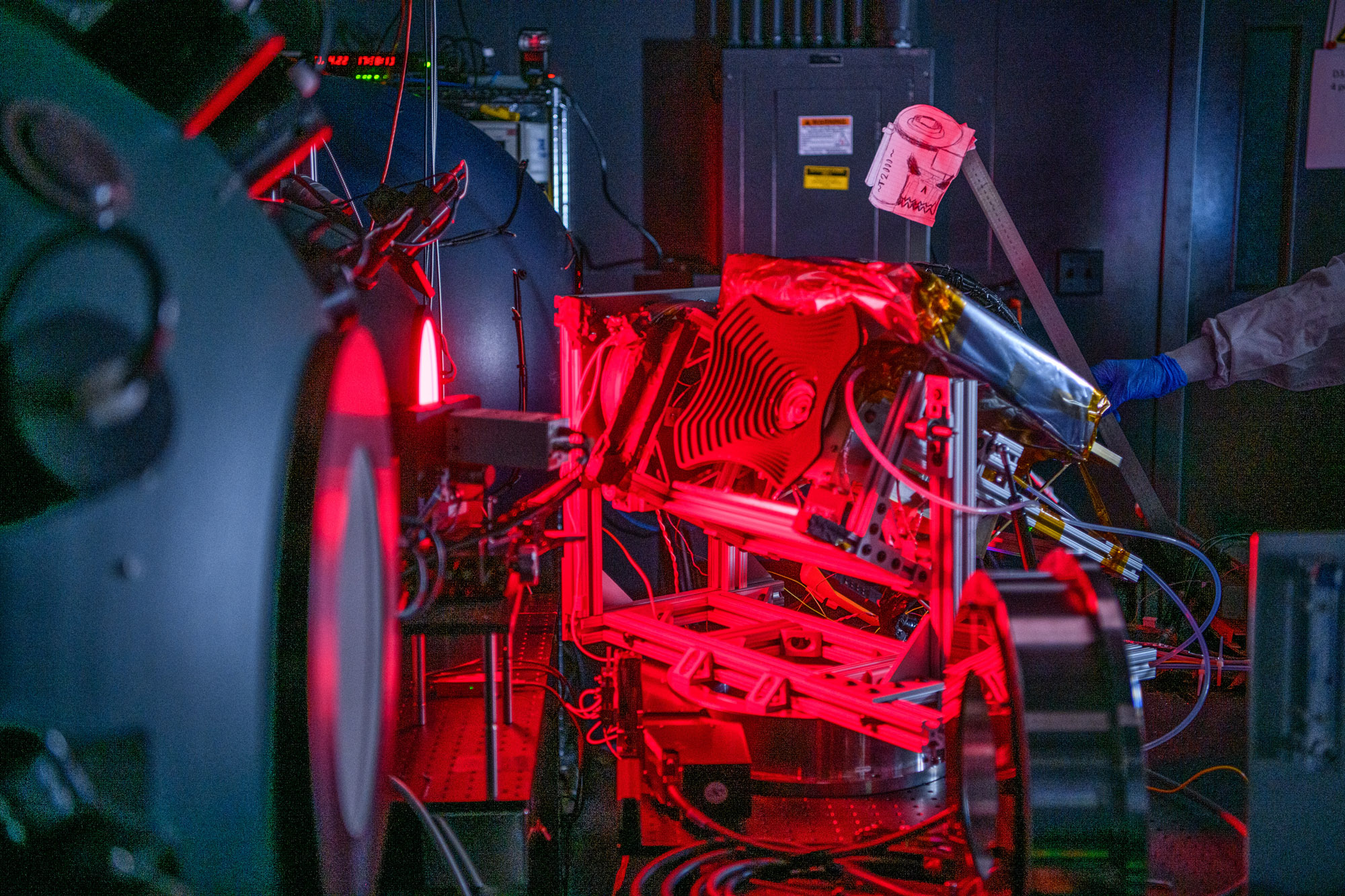 A small piece of spaceflight hardware in a dark room, exposed to a bright red light for calibration testing prior to launch