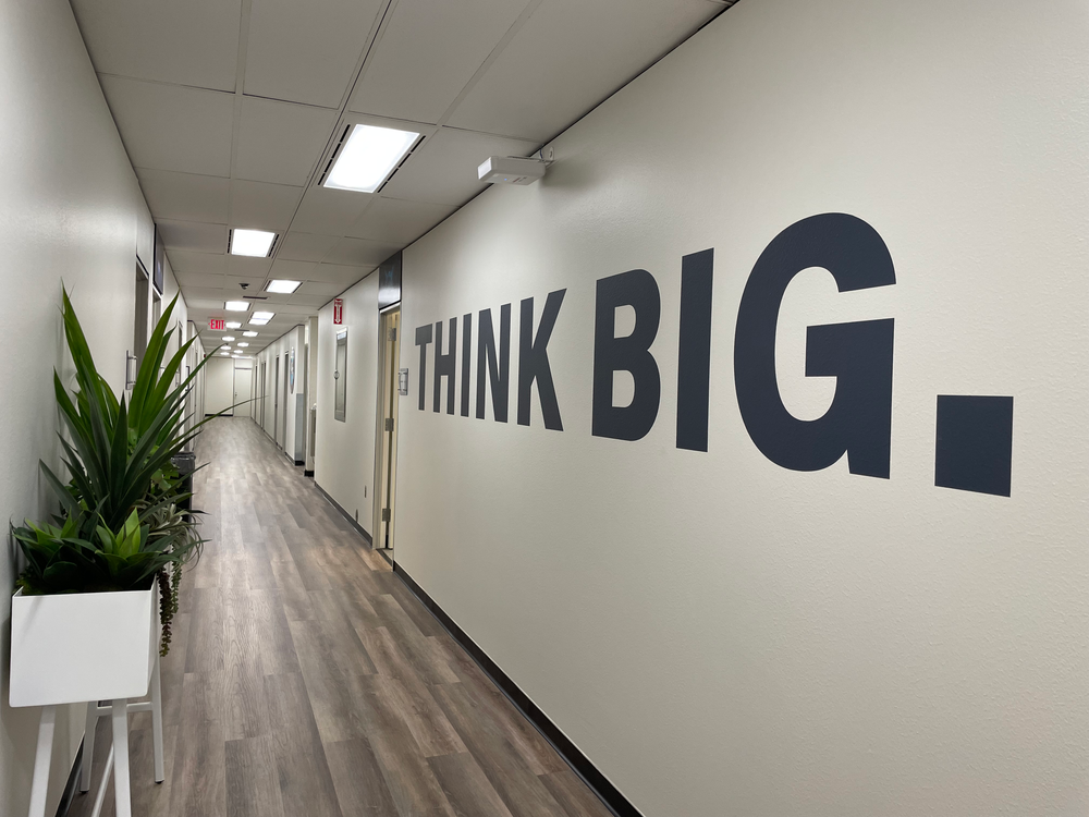 A hallway in an office building with white walls and black letters that read, "Think Big."
