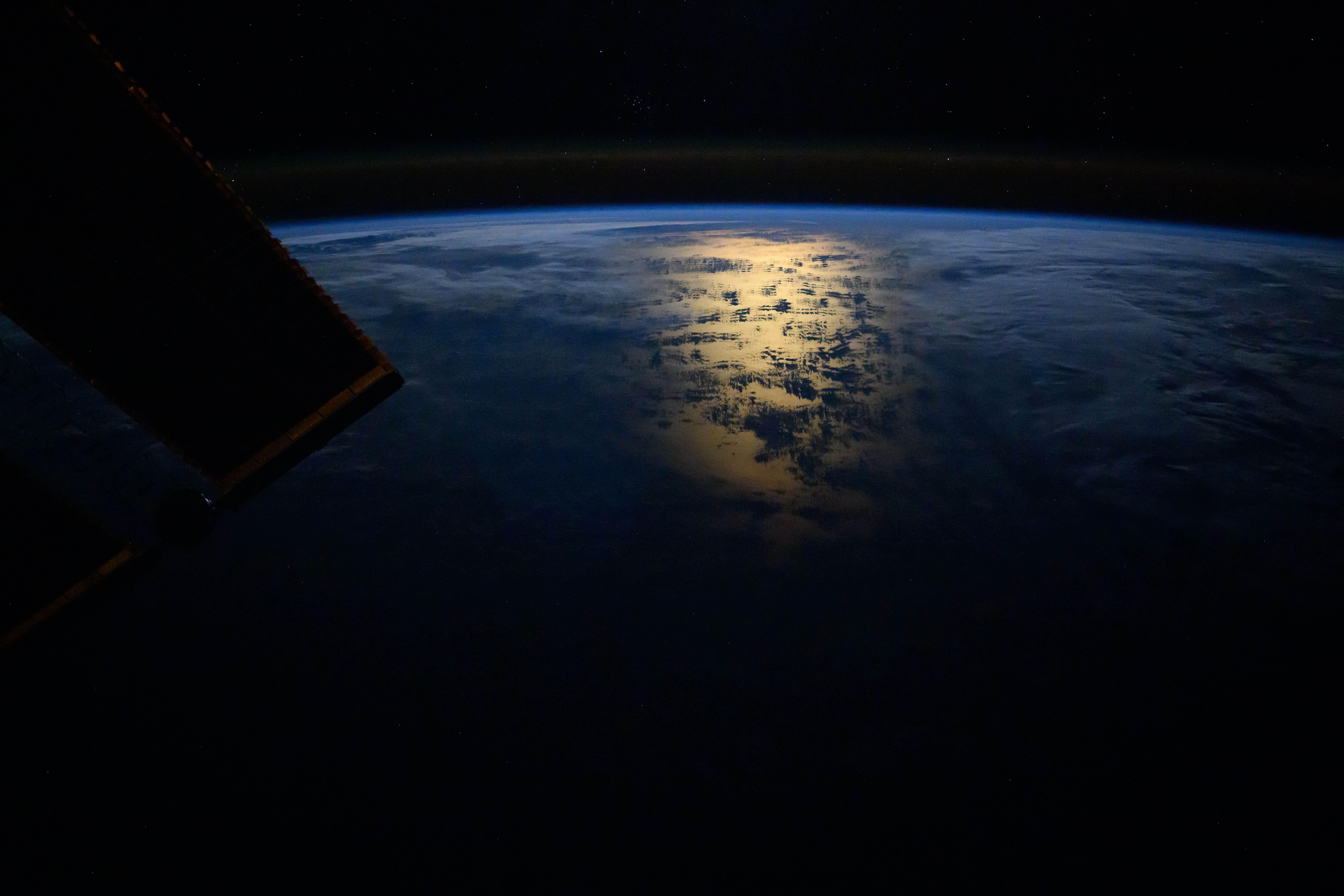 The Sun's glint beaming off the South Pacific Ocean near the coast of Chile just after an orbital sunrise and a slight airglow crowning Earth's horizon are photographed from the International Space Station. At top, are star fields including a cluster of stars in the constellation of Cancer and a portion of the Lynx constellation.