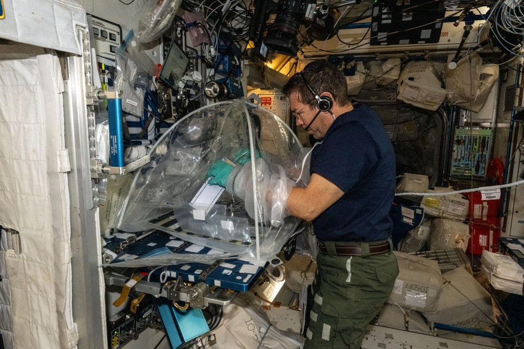 Expedition 70 Flight Engineer and NASA astronaut Mike Barratt works aboard the International Space Station's Harmony module processing protein crystal samples inside a portable glovebag to learn how to generate personalized medicines in space for astronauts.
