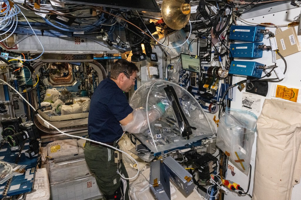 Expedition 70 Flight Engineer and NASA astronaut Mike Barratt works aboard the International Space Station's Harmony module processing protein crystal samples inside a portable glovebag to learn how to generate personalized medicines in space for astronauts.