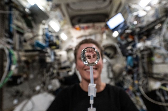 Expedition 70 Flght Engineer and NASA astronaut Loral O'Hara's image is refracted in a water bubble she squeezed from a drinking bag aboard the International Space Station's Kibo laboratory module.