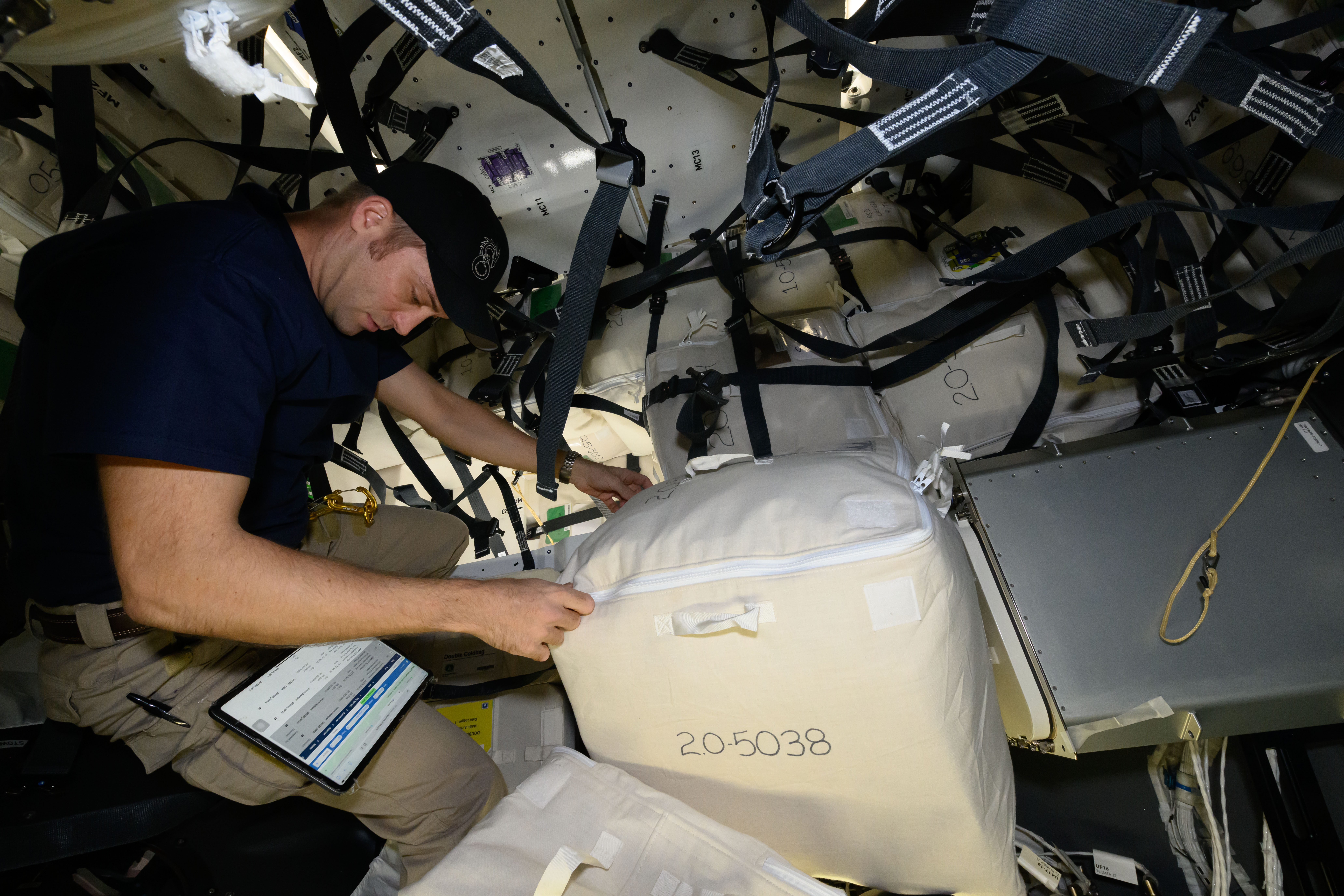 Expedition 71 Flight Engineer and NASA astronaut Matthew Dominick checks procedures on a computer tablet while loading cargo for return to Earth inside the SpaceX Dragon spacecraft.