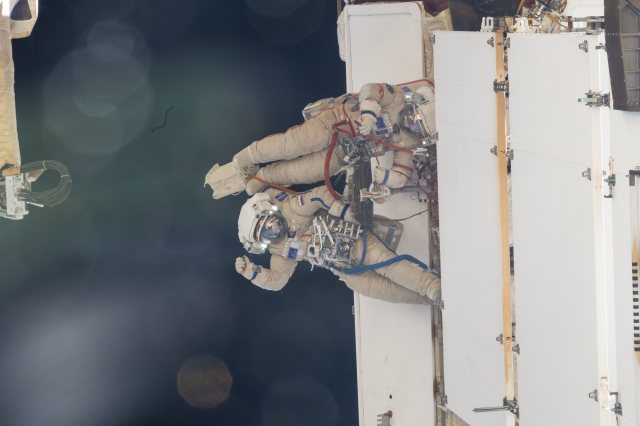 Cosmonauts Nikolai Chub (waving) and Oleg Kononenko are pictured outside of the International Space Station wearing their Orlan spacesuits during a four-hour and 36-minute spacewalk. During their excursion they worked on the Russian segment of the complex completing the deployment of one panel on a synthetic radar communications system. The duo also installed equipment and experiments to analyze the level of corrosion on station surfaces and modules.