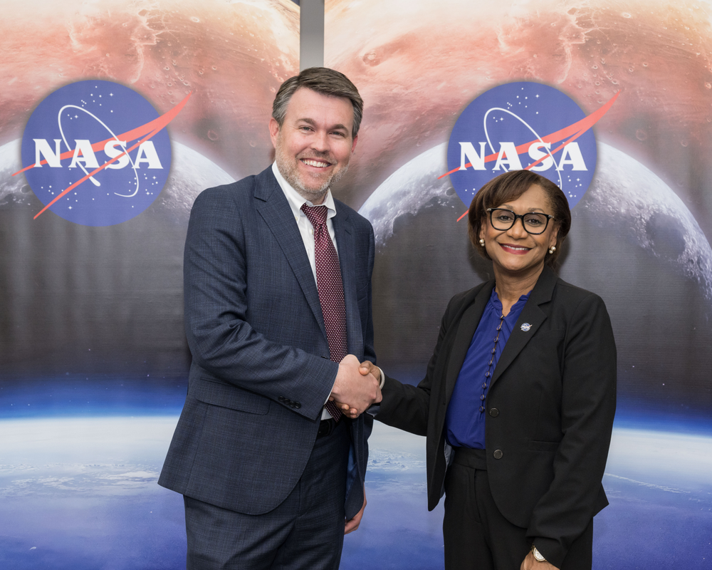 American Center for Manufacturing and Innovation Founder and CEO John Burer, with brown hair and wearing as suit and tie, shakes hands with NASA’s Johnson Space Center Director Vanessa Wyche, wearing a black suit with a blue shirt
