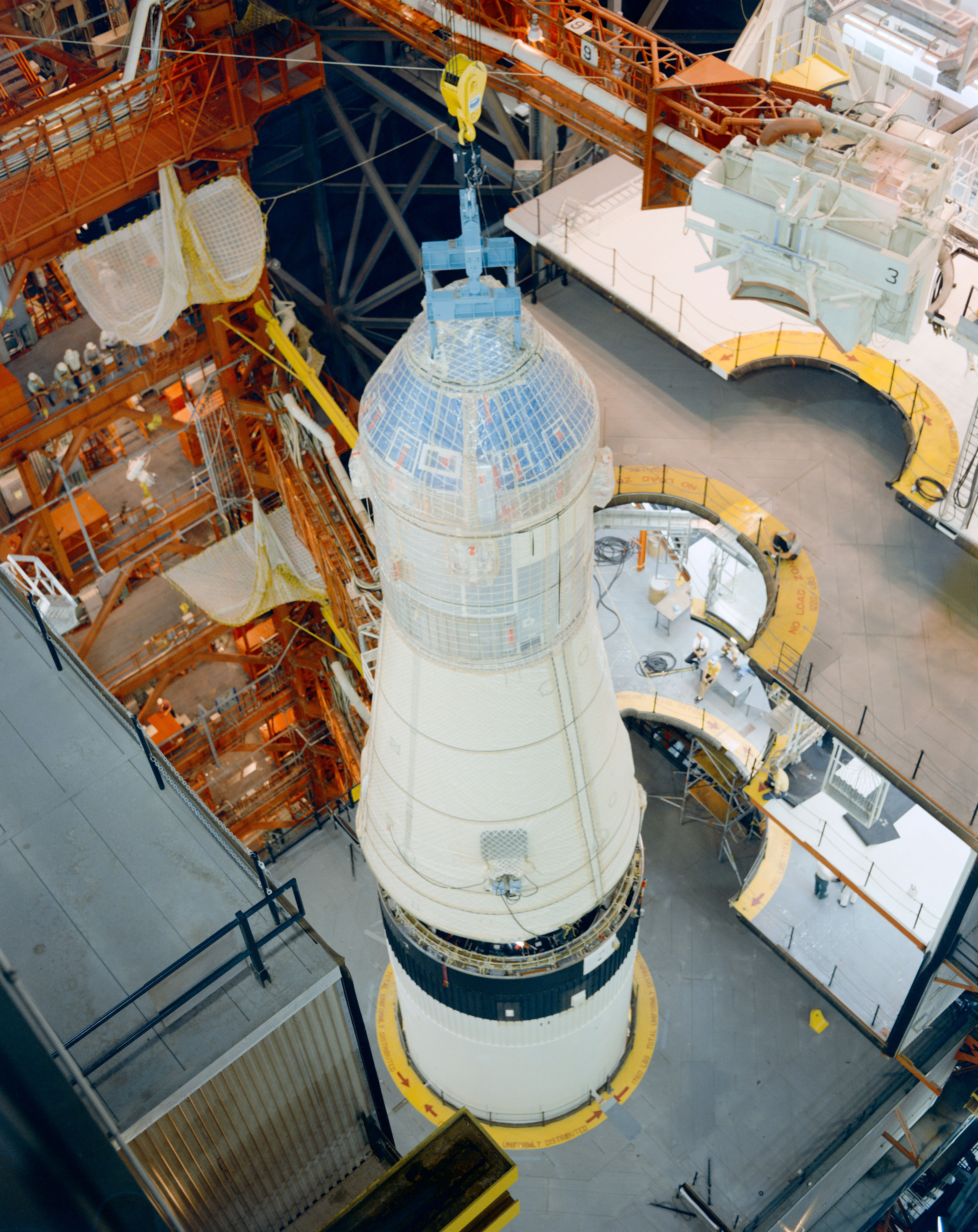 In KSC's Vehicle Assembly Building, workers lower the Apollo 11 spacecraft onto its Saturn V rocket