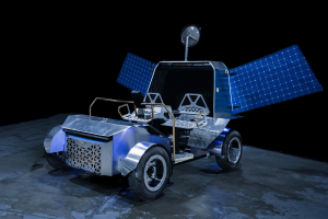A full-scale prototype lunar terrain vehicle sits on a dark studio floor against a black background. The vehicle has four wheels, two crew seats, deployed blue solar arrays extending from both sides, and a communications dish mounted above the rear section.