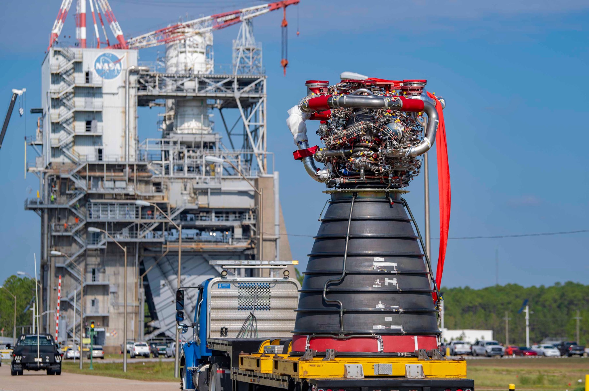 an RS-25 is seen on the back of a large truck; The Fred Haise Test Stand is visible in the background