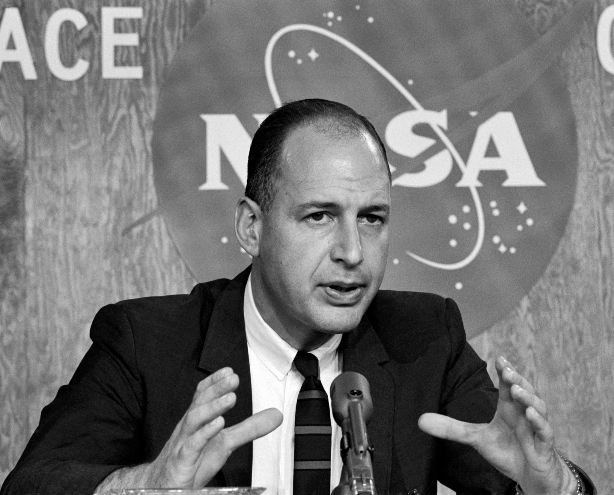 Man seated in front of NASA insignia.