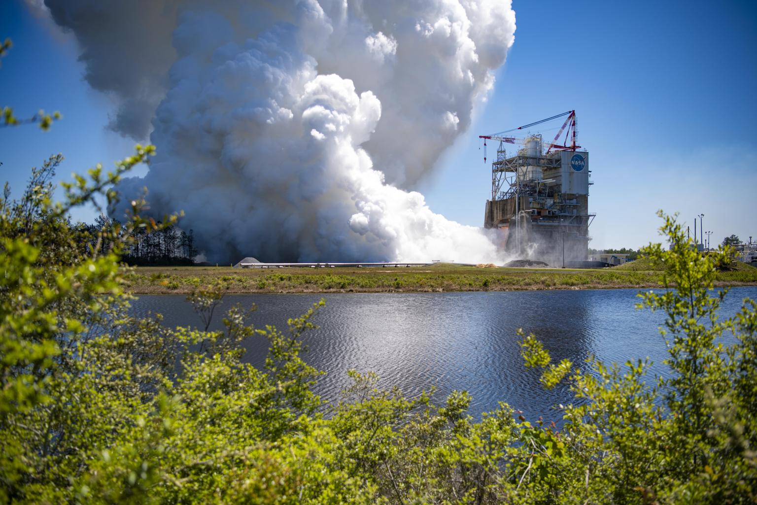 a RS-25 hot fire is seen across the canal at NASA Stennis Test Complex; cover for April 2024 Lagniappe