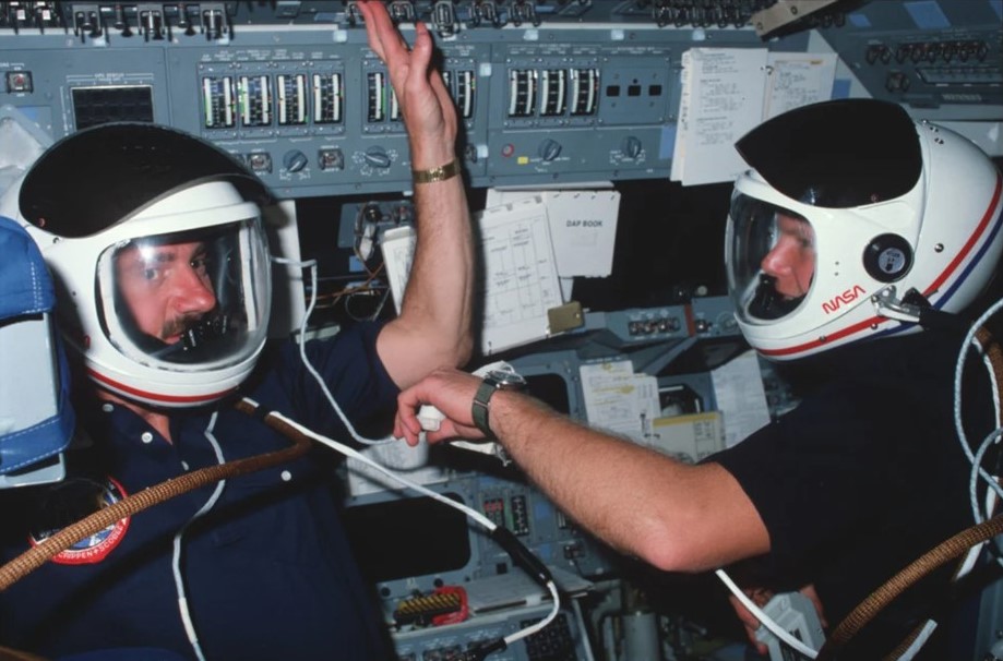 STS-41C astronauts James D. “Ox” Van Hoften, left, and George D. “Pinky” Nelson wear their launch and entry helmets during the prebreathe for the first spacewalk