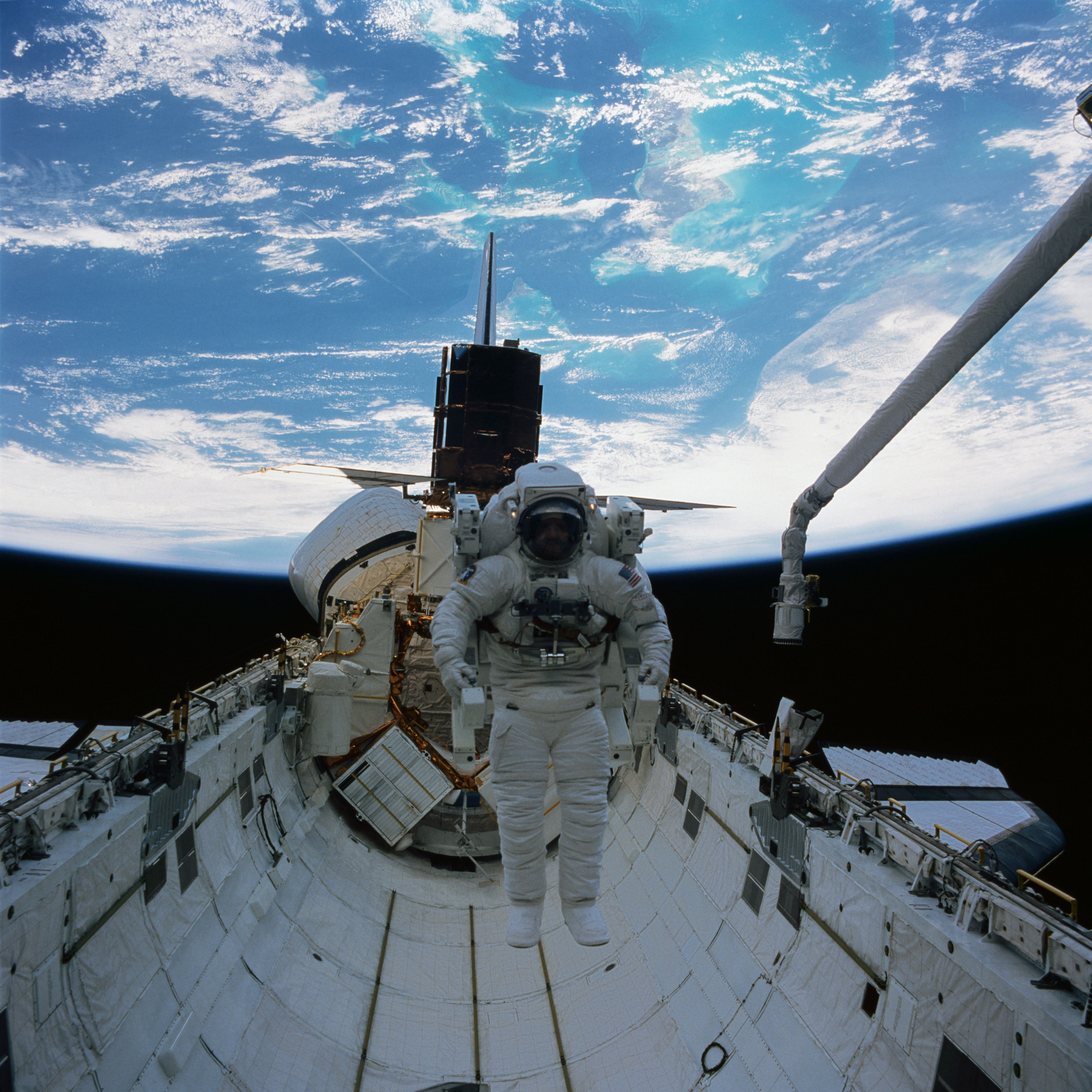 During the second STS-41C spacewalk, James D. “Ox” Van Hoften flies the Manned Maneuvering Unit in Challenger’s payload bay