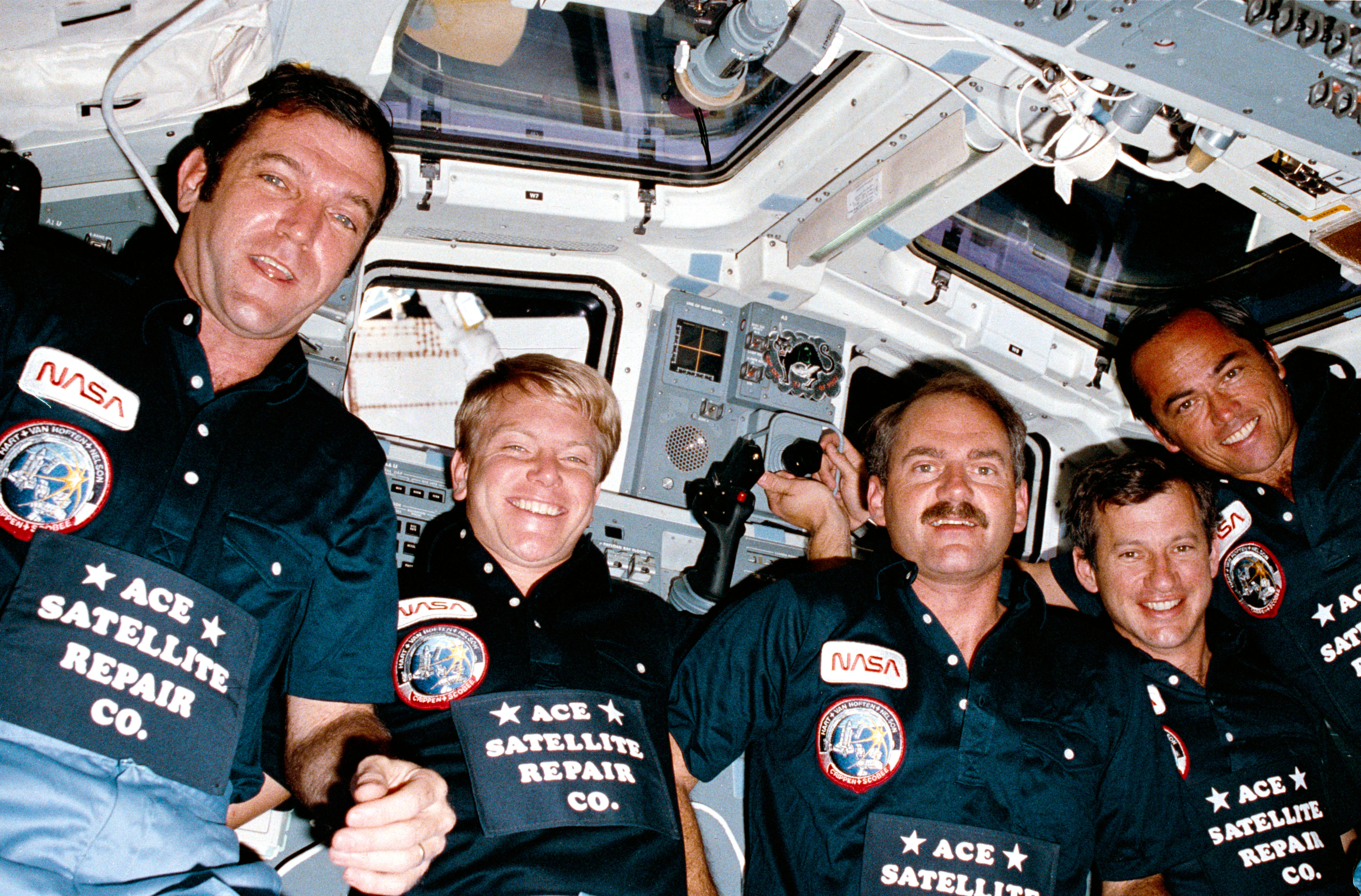 The STS-41C crew members pose on Challenger's flight deck near the end of their successful mission, wearing customized shirts