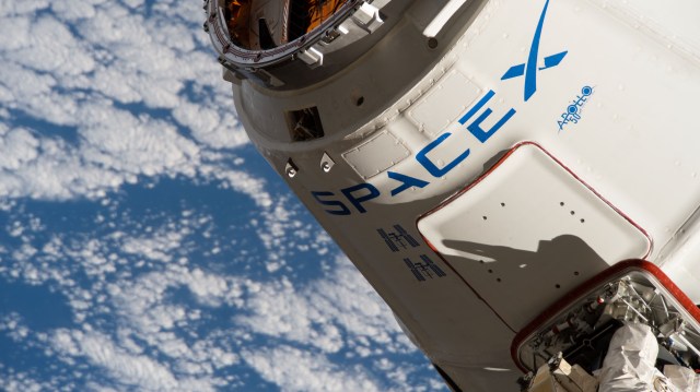 iss060e014962 (July 27, 2019) --- The reusable SpaceX Dragon space freighter is in the grips of the Canadarm2 robotic arm shortly after it was captured following a day-and-a-half-long trip that began with a launch from Cape Canaveral, Florida. This was the third flight of this spacecraft with its previous flights denoted by two insignia depicting the International Space Station. The Apollo 50th anniversary insignia is also highlighted on the commercial resupply ship.