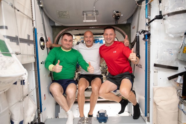 iss060e013847 (July 22, 2019) -- Three Expedition 60 crewmembers pose for a portrait inside the vestibule between the Columbus laboratory module and the Harmony module. From left are Alexey Ovchinin of Roscosmos; Luca Parmitano of the European Space Agency; and Drew Morgan of NASA.