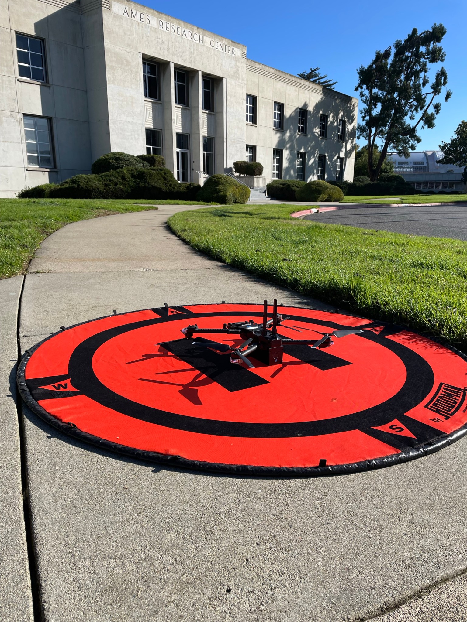 Four rotor drone on orange landing pad in front of building at Ames Research Center.