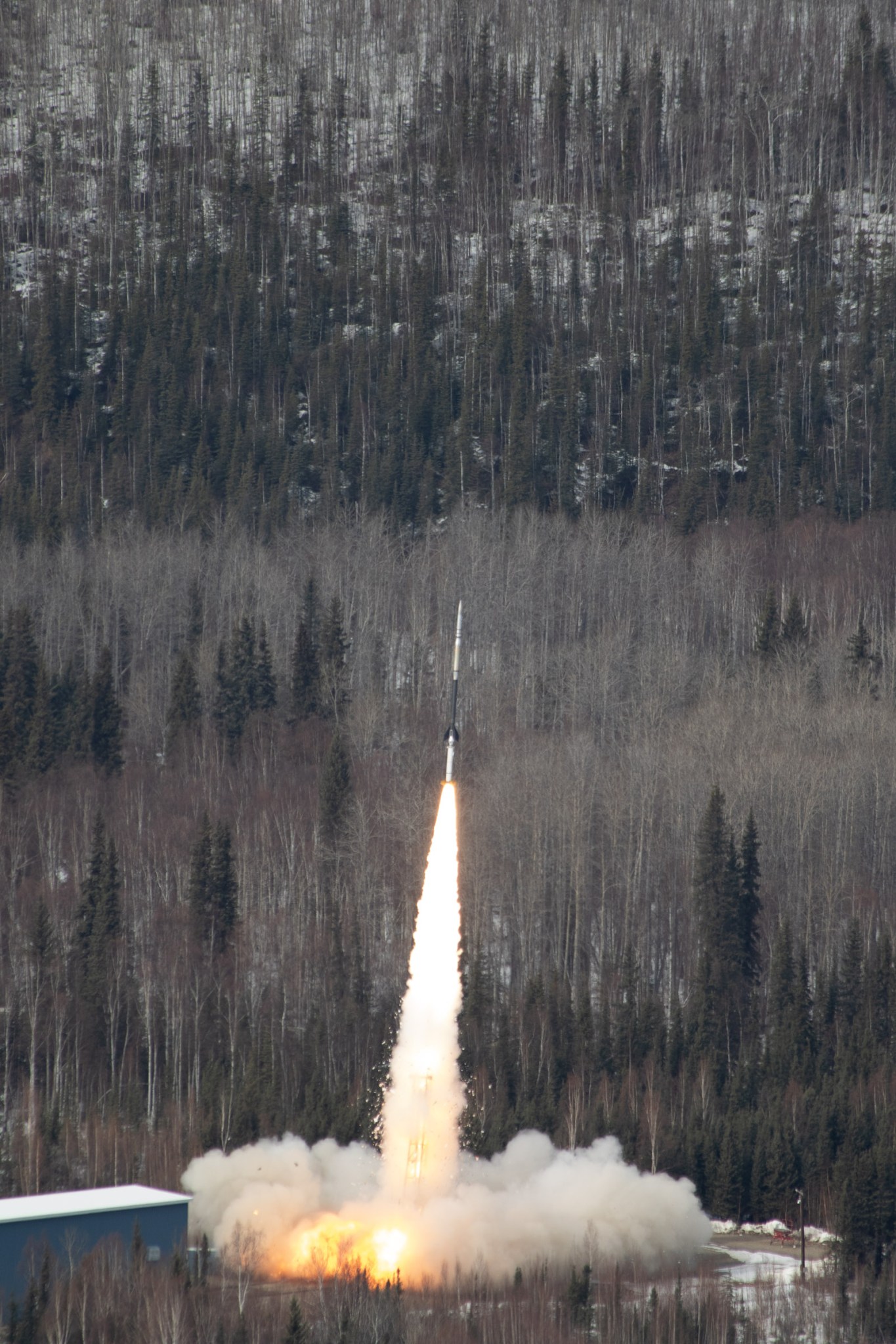 A sounding rocket just seconds after launch with a bright white plume of smoke trailing underneath against a muted snowy landscape.