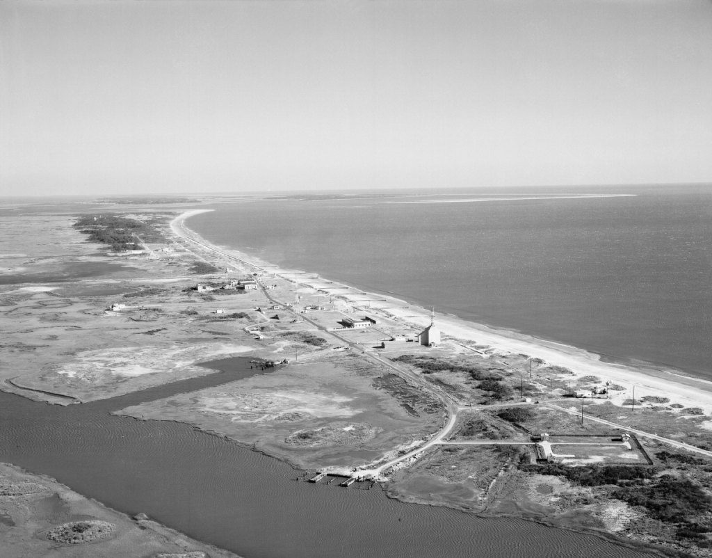 1961 Black and white image of support buildings and roads, ocean groins (east), and marsh (west) ferry docks on Wallops Island, Virginia.