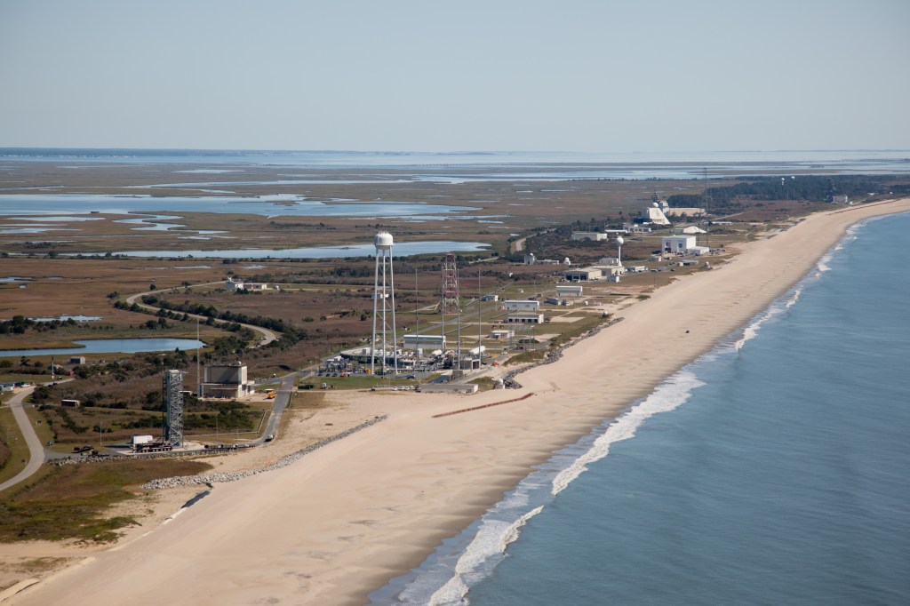 Island with NASA Wallops launch range in the foreground and support buildings and roads going north. Marshes to the west and newly restored sandy beach to the east.