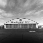 Black and white photo of the Glenn Research Center hangar that is in the distance. Clouds above the hangar look like they are moving fast.