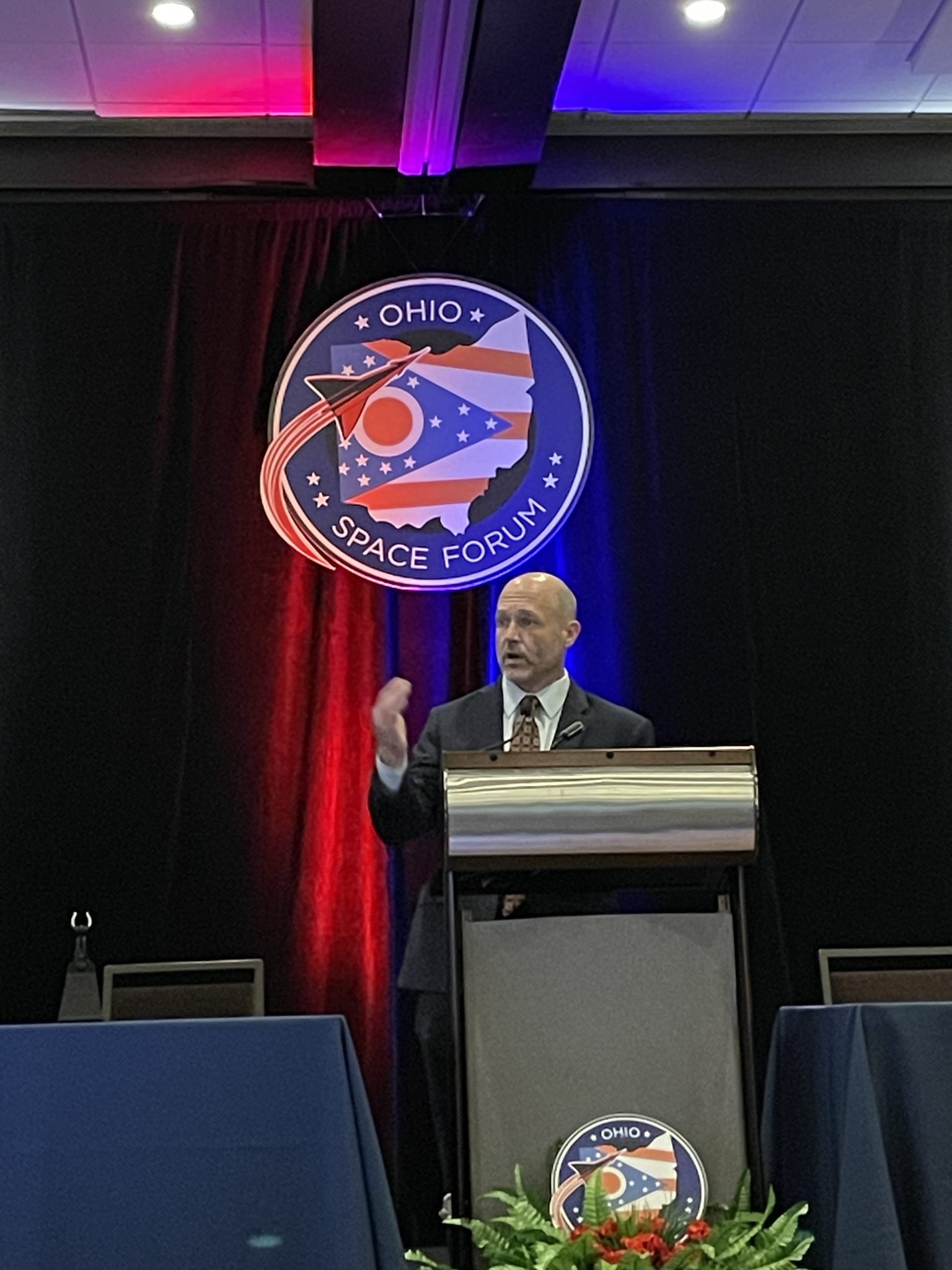 The NASA Glenn center director gives a speech at a podium by a large logo of the Ohio Space Forum.