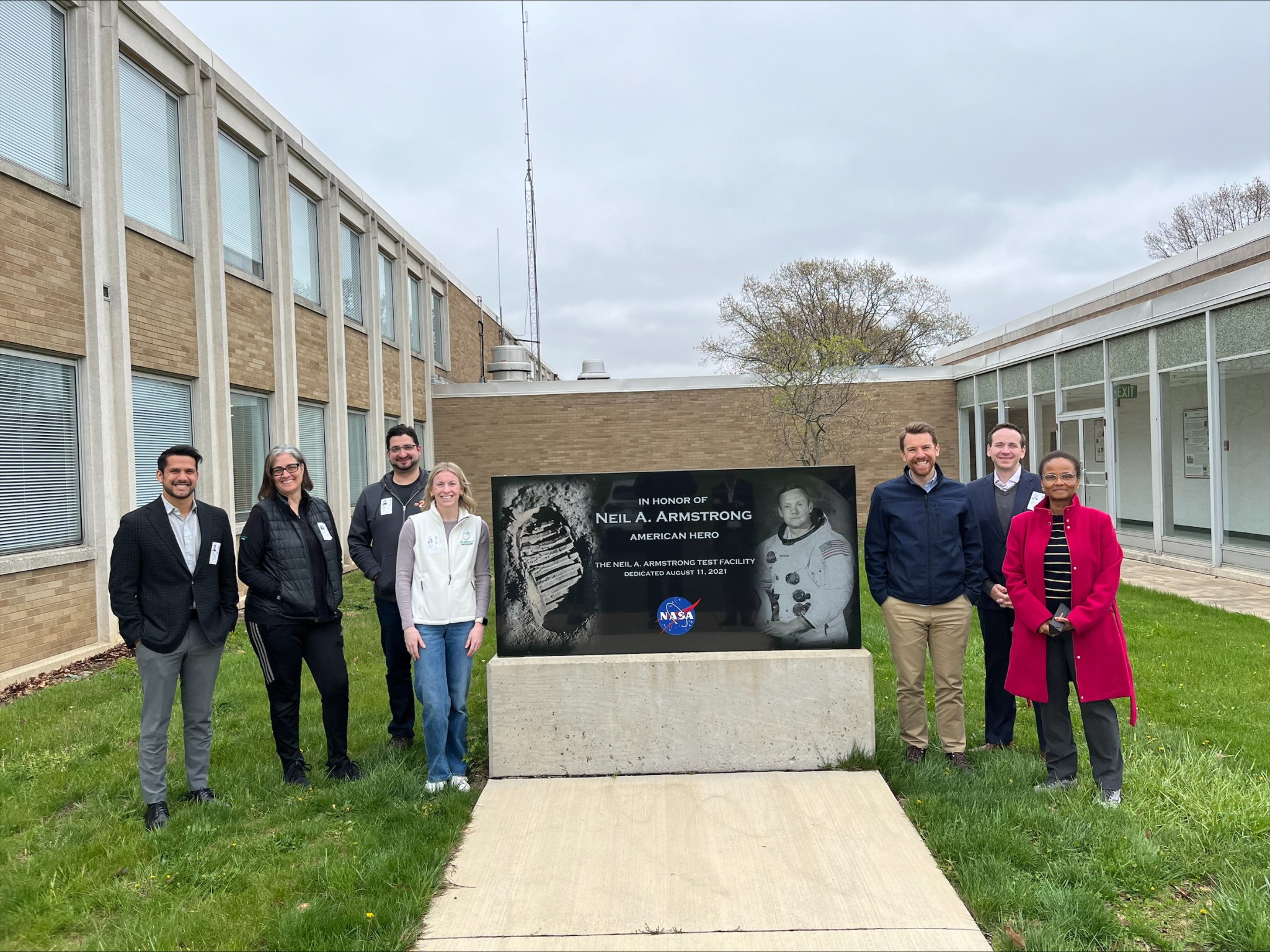 Four people stand on each side of a large marble monument, which reads “In Honor of Neil A. Armstrong, American Hero, The Neil A. Armstrong Test Facility, Dedicated August 11, 2021.