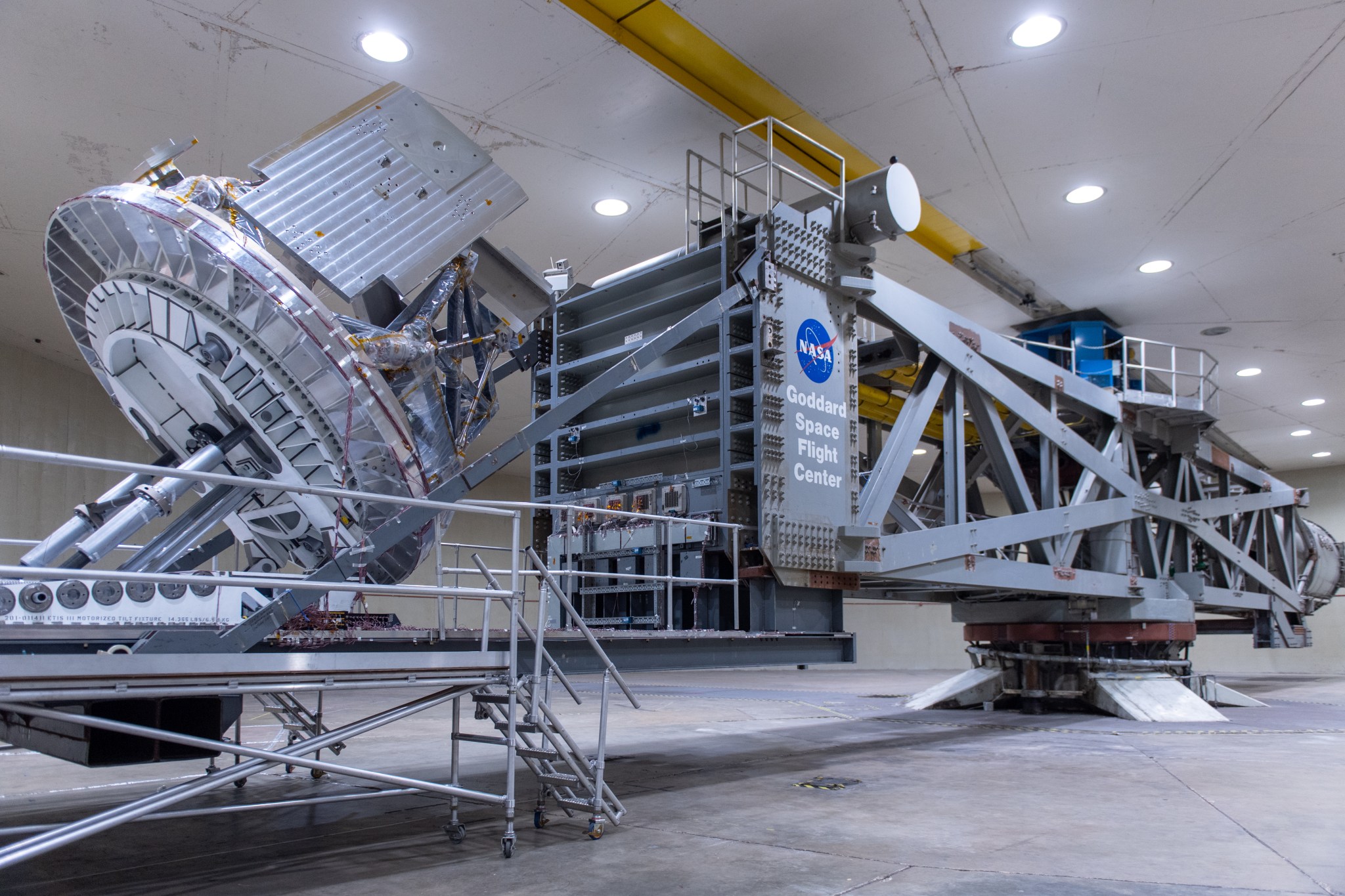 A large centrifuge at Goddard Space Flight Center. The centrifuge is a light grey metal metal structure with a platform on the end that holds a piece of instrumentation. 