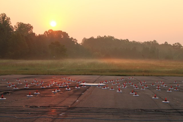 An array of microphones on the an airfield, with a sunrise in the background