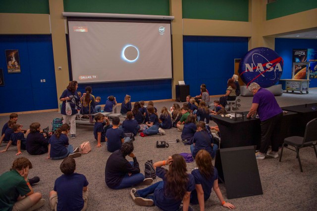 Schoolchildren watching a live television broadcast of the eclipse while sitting in the atrium at INFINITY Science Center