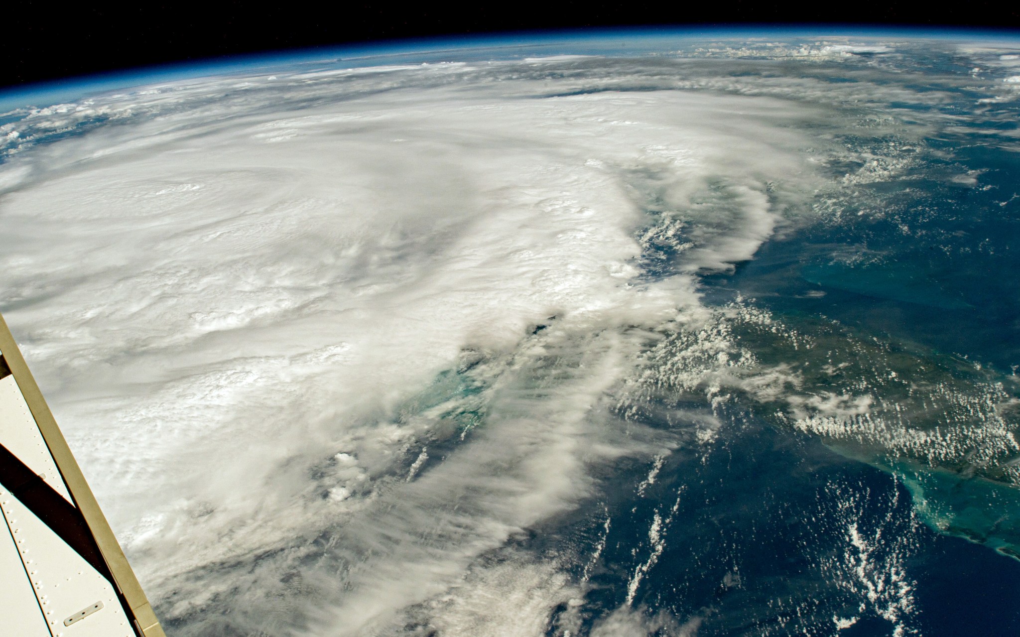 Hurricane Idalia as seen from the International Space Station looks like a huge, sprawling white circular cloud. It dominates the image, with the water of the Gulf of Mexico mostly visible in the bottom right portion of the photo. Also at bottom right is part of Cuba. At top is some of Earth's curvature and at bottom left is part of the space station.