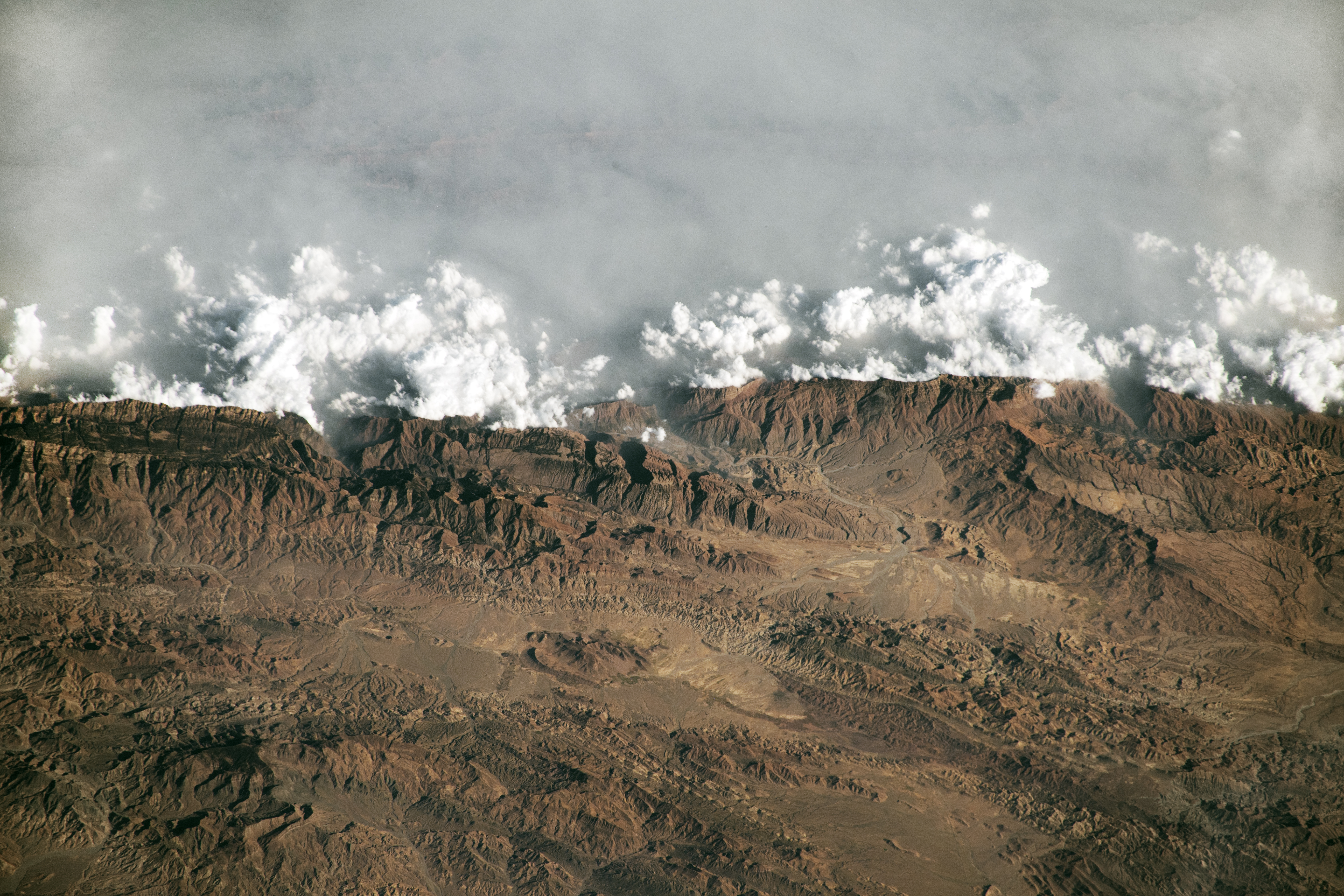 A wall of gray haze meets the brown Sulaiman Mountains, looking almost like waves crashing on a beach.