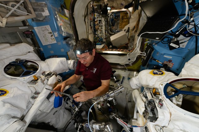 NASA astronaut and Expedition 71 Flight Engineer Mike Barratt reads maintenance procedures on a computer tablet as he works on a pair of spacesuits inside the International Space Station's Quest airlock.