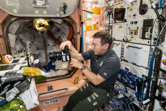 NASA astronaut and Expedition 71 Flight Engineer Mike Barratt photographs food packs in the Unity module's galley aboard the International Space Station.
