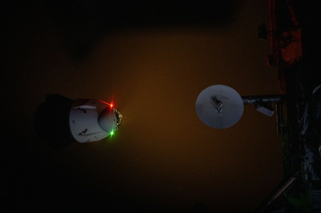 The SpaceX Dragon Endeavour spacecraft's navigation lights and engine plume during an engine firing illuminate the darkness of space as it backs away from the International Space Station. Dragon switched ports moving from the Harmony module's forward port to its space-facing port during the relocation maneuver.