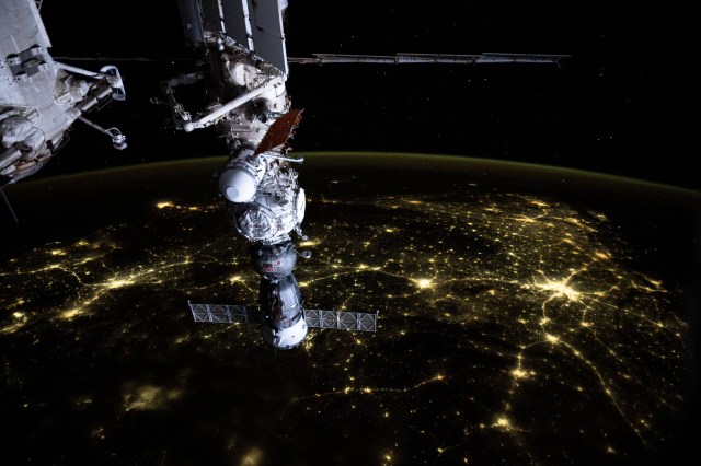 An atmosphreric glow blankets Earth's horizon and a web of city lights interconnect across India in this photograph from the International Space Station as it soared 256 miles above the subcontinent. In the foreground, the Soyuz MS-25 crew ship is pictured docked to the Prichal docking module which is itself attached to the Nauka science module.