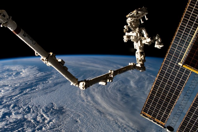 The Canadarm2 robotic arm with its fine-tuned robotic hand, also known Dextre, attached extends into the frame with a set of main solar arrays draping downward (right) as the International Space Station orbited 267 miles above a cloudy South Atlantic Ocean off the coast of Argentina.