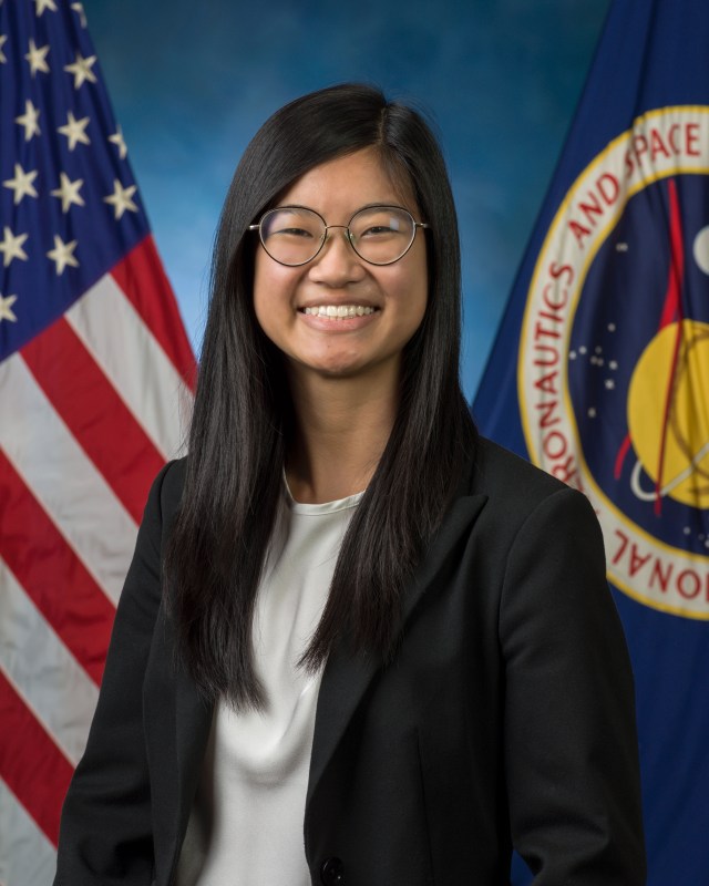 Professional portrait of a young Asian American woman wearing glasses, a black blazer, and a white silk shirt.
