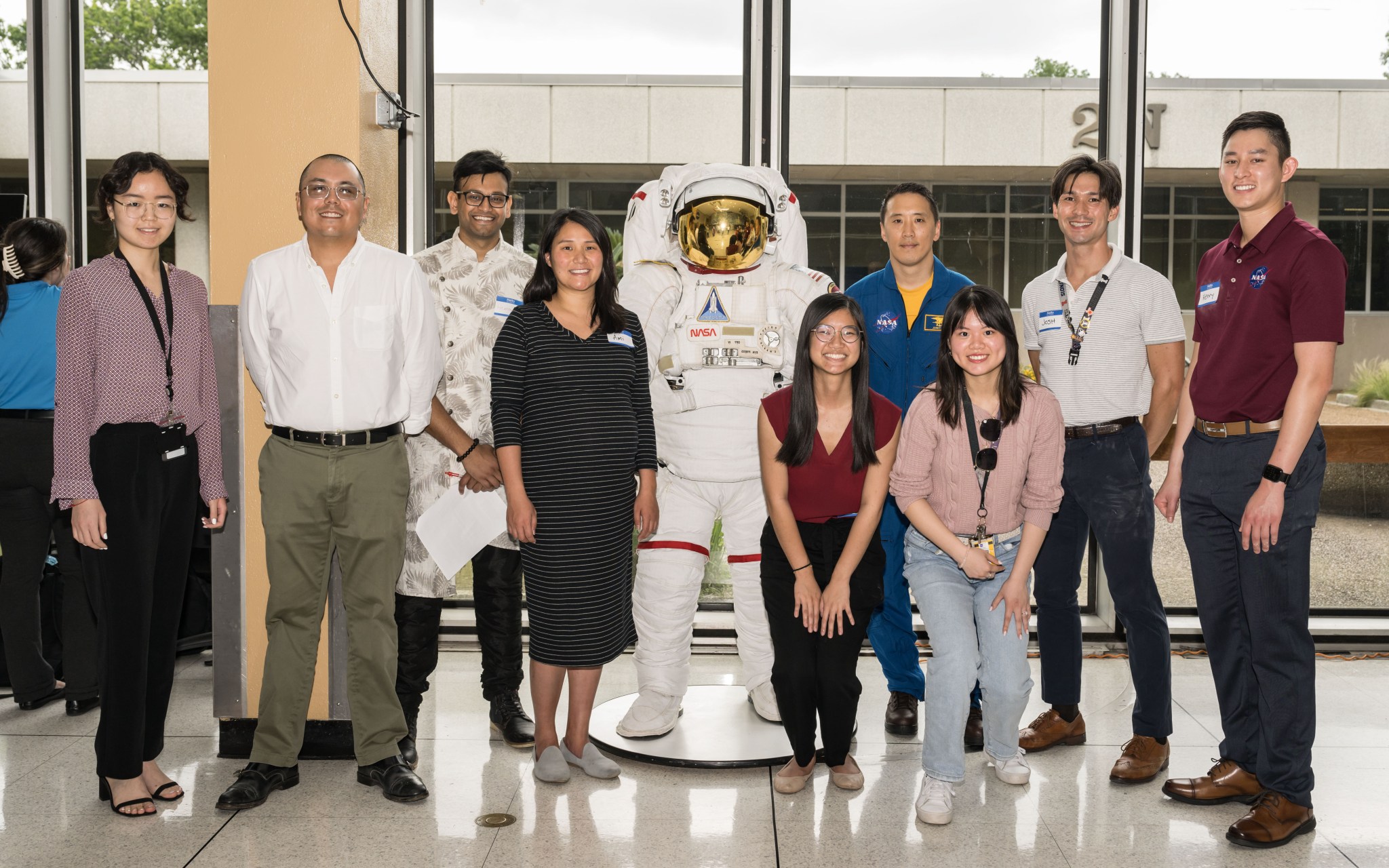 A group of eight male and female Asian American individuals pose for a photograph with NASA astronaut Jonny Kim and a spacesuit.